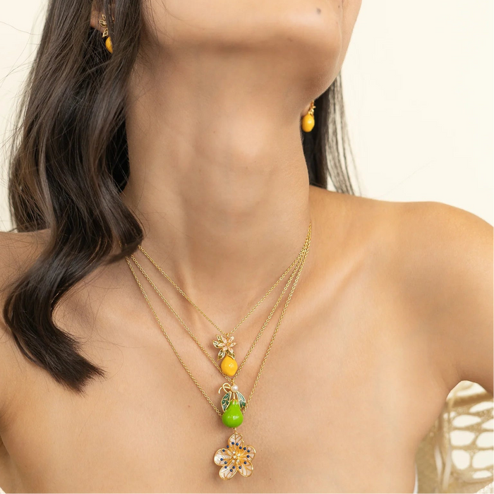 Woman wearing a stack of Brass Necklaces with a floral and fruit enamelled pendants finished in 22k gold